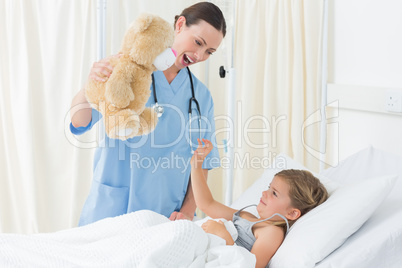Doctor entertaining sick girl with teddy bear