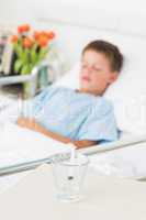 Syringe in glass with boy resting in hospital ward