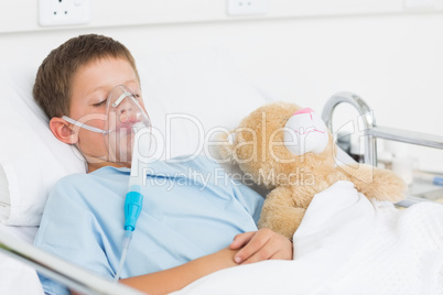 Boy wearing oxygen mask sleeping beside teddy bear