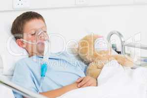 Boy wearing oxygen mask sleeping beside teddy bear