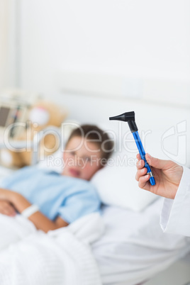 Doctor holding otoscope with boy in hospital