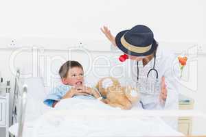 Doctor entertaining sick boy in hospital bed