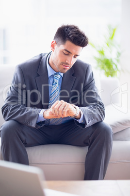 Smiling businessman sitting on the sofa checking his watch