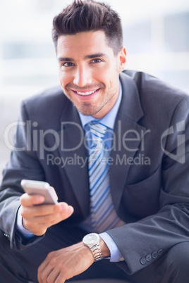 Happy businessman sitting on sofa sending a text