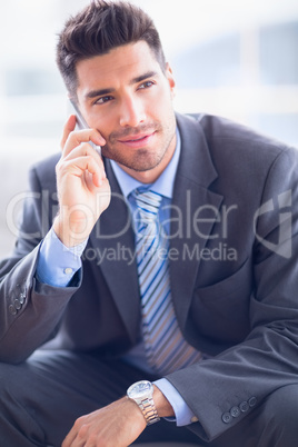 Happy businessman sitting on sofa making a call