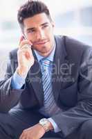 Happy businessman sitting on sofa making a call
