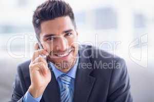 Handsome businessman sitting on sofa making a call smiling at ca