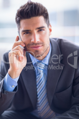 Businessman sitting on sofa making a call smiling at camera