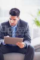 Businessman sitting on sofa using his tablet pc