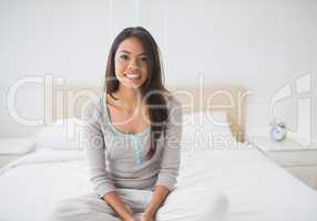 Pretty girl sitting on bed smiling at camera