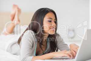 Pretty girl lying on bed using her laptop