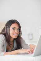 Happy girl lying on bed using her laptop smiling at camera