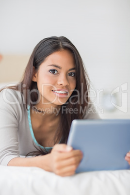 Happy girl lying on bed using her tablet pc smiling at camera