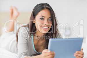 Pretty girl lying on bed using her tablet pc smiling at camera