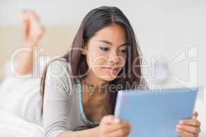 Pretty girl lying on bed using her tablet pc