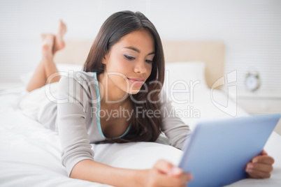 Pretty girl lying on bed using her digital tablet