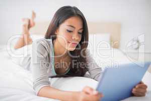 Pretty girl lying on bed using her digital tablet