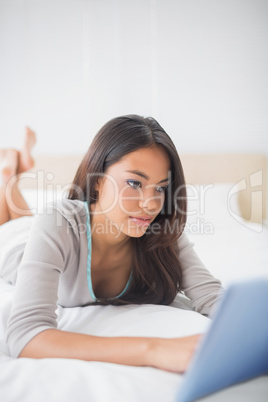 Pretty girl lying on bed using her tablet