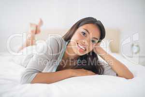 Pretty girl lying on bed smiling at camera