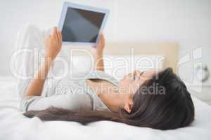 Pretty young girl lying on bed looking at her tablet pc