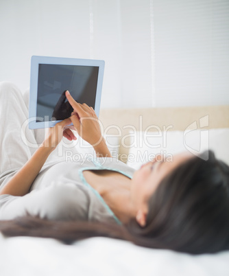 Young girl lying on bed looking up at her tablet pc