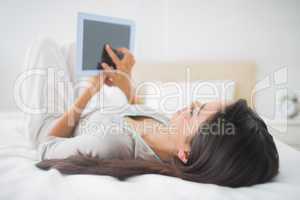 Young girl lying on bed looking at her tablet pc