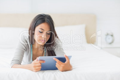 Young pretty girl lying on her bed using her tablet