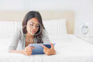 Young pretty girl lying on her bed using her tablet