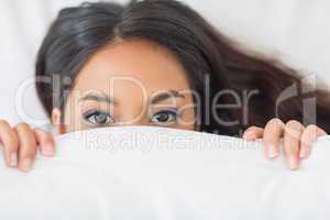 Young girl peeking from under the duvet