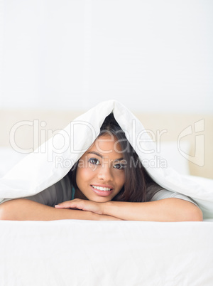 Happy girl lying under the duvet smiling at camera