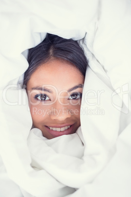 Happy girl wrapped up in her duvet smiling at camera