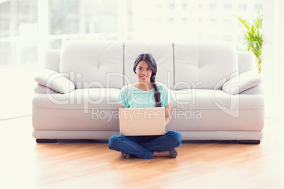 Pretty girl sitting on floor using laptop smiling at camera