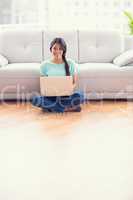 Pretty girl sitting on a floor using laptop smiling at camera