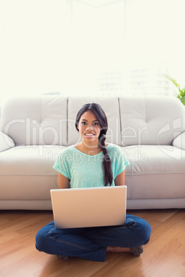 Young girl sitting on floor using her laptop smiling at camera