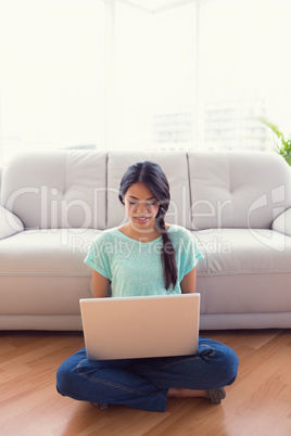 Young smiling girl sitting on floor using her laptop