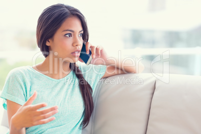 Serious girl sitting on sofa making a phone call