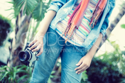 Woman wearing jeans and denim shirt holding camera outside