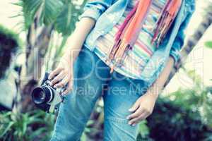 Woman wearing jeans and denim shirt holding camera outside