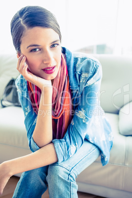 Pretty brunette sitting on sofa smiling at camera