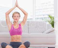 Fit blonde meditating in lotus pose with arms raised