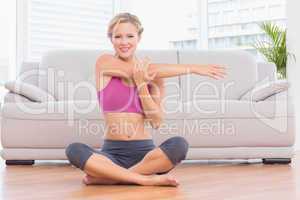 Smiling blonde sitting in lotus pose stretching arms