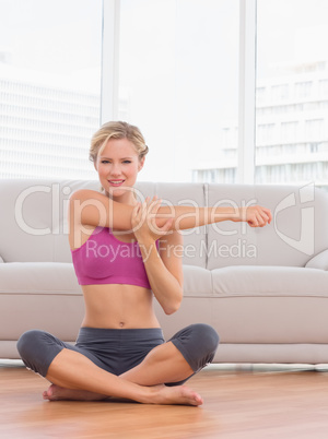 Happy blonde sitting in lotus pose stretching arms