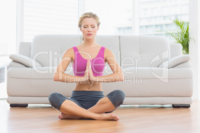 Calm blonde sitting in lotus pose with hands together