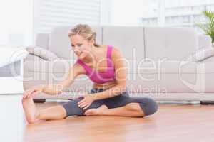 Fit blonde sitting on floor stretching her leg