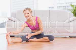 Smiling blonde sitting on floor stretching her leg