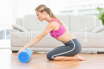 Fit blonde kneeling on floor using foam roller