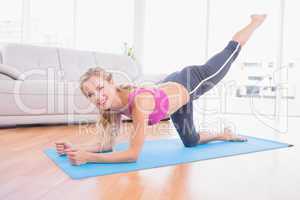 Toned blonde doing pilates on exercise mat smiling at camera