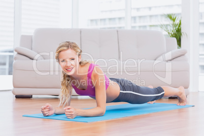 Fit blonde in plank position on exercise mat smiling at camera