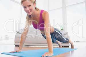 Strong blonde in plank position on exercise mat smiling at camer