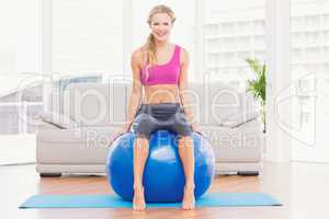 Fit blonde sitting on exercise ball smiling at camera